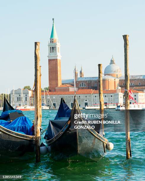group of two italian gondolas tied up at some posts of the dock while they are floating on the blue sea at the sunset. at the back there is the amazing venetian island of san giorgo maggiore - gondola traditional boat stockfoto's en -beelden