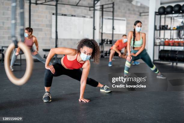 latin woman working out at the gym wearing protective face mask and looking at camera - gym reopening stock pictures, royalty-free photos & images