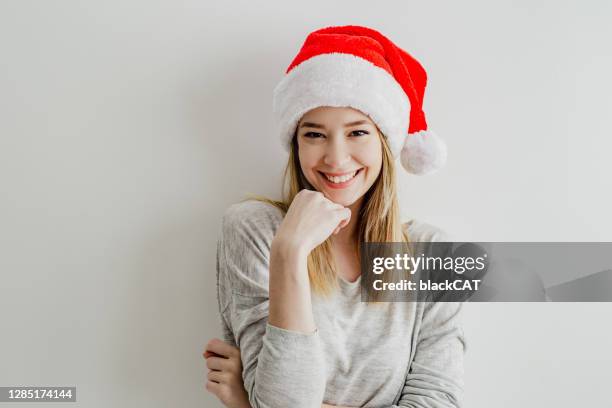 portrait of a young woman in front of a white wall with a santa hat - santa face stock pictures, royalty-free photos & images