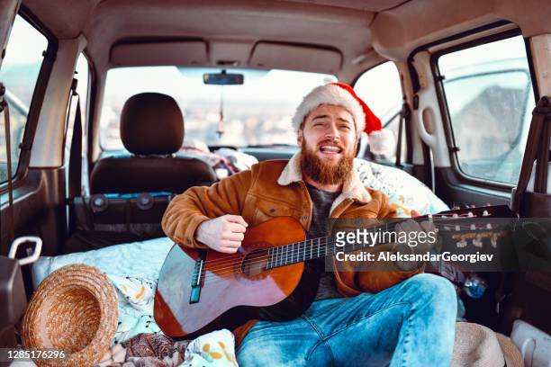 male with santa hat playing guitar in minivan - acoustic christmas stock pictures, royalty-free photos & images