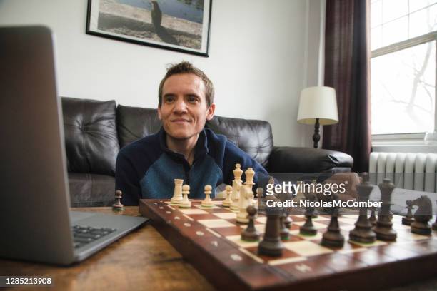 Quarantined man playing chess with friend using video conference on laptop
