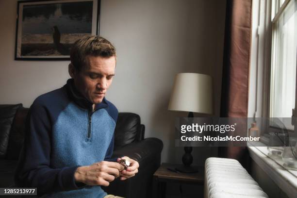 autistic trans man at home working on handheld puzzle by window - autistic adult imagens e fotografias de stock