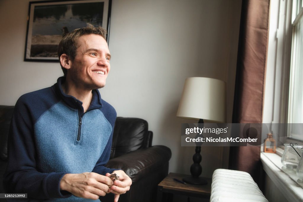 Autistic trans man at home smiling as he looks out of the window