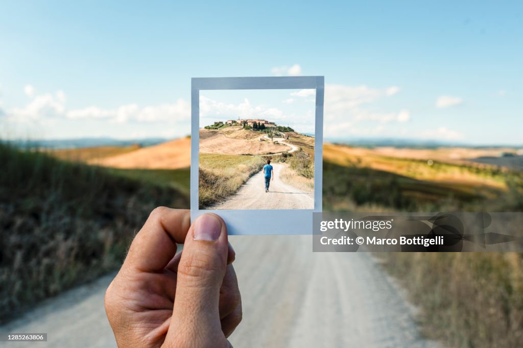 Personal perspective of polaroid picture overlapping a country road in Tuscany
