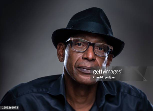 real man with a serious expression. portrait of a real man with black hat on a gray background. - only mid adult men stock pictures, royalty-free photos & images