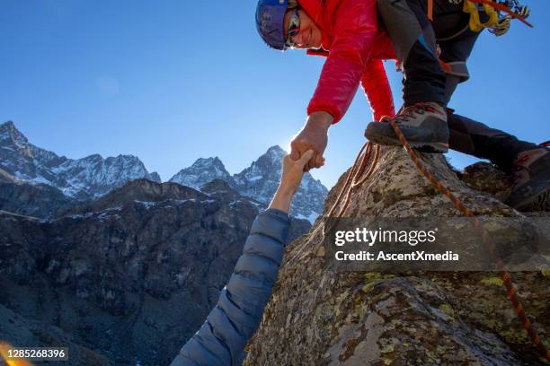 mountaineer offers helping hand to companion - women rock climbing stock pictures, royalty-free photos & images