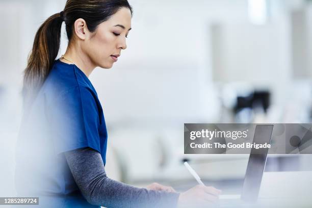 female nurse working with laptop at desk - medical scrubs - fotografias e filmes do acervo