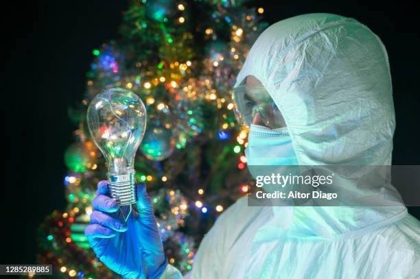 scientist gazes at a light bulb that he holds in his hand. christmas tree in the background. - patenturkunde stock-fotos und bilder