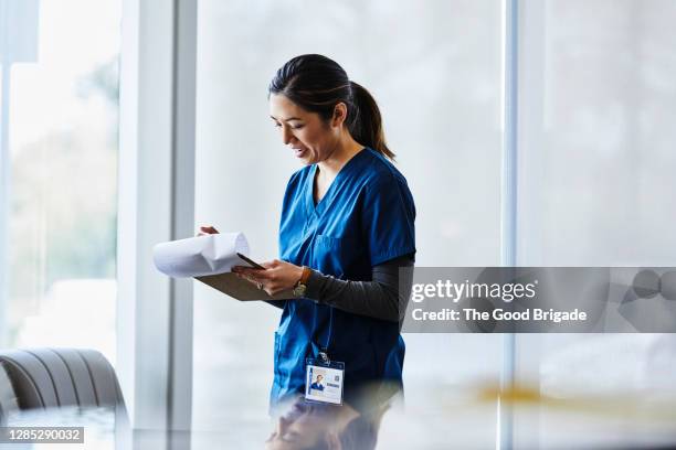 smiling female nurse examining document in hospital lobby - medical occupation ストックフォトと画像