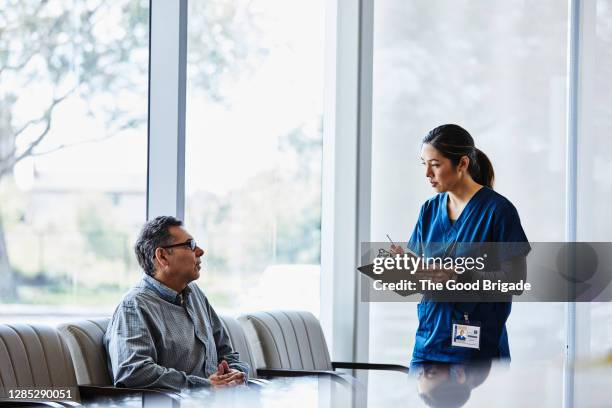 nurse talking with senior male patient sitting in lobby at hospital - outpatient care stock pictures, royalty-free photos & images