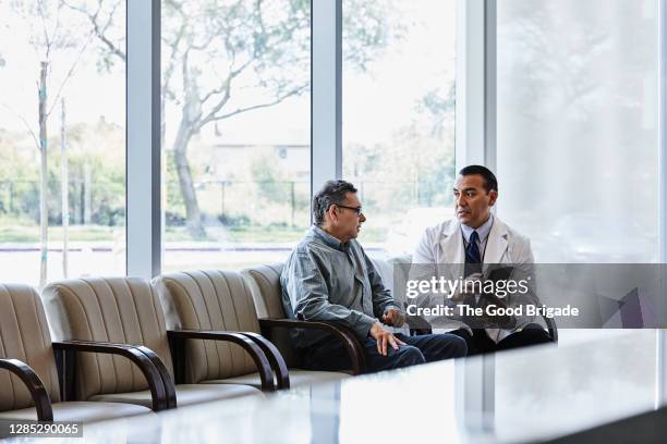 doctor with digital tablet discussing with male patient in waiting room - male doctor man patient stockfoto's en -beelden