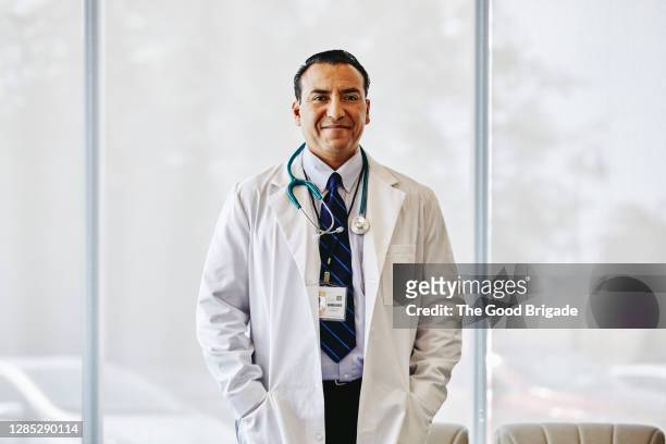 portrait of confident male doctor standing in hospital lobby - arzt portrait stock-fotos und bilder