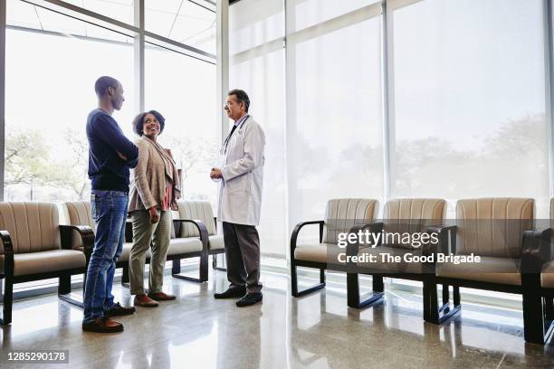 doctor talking to mother and adult son in hospital waiting room - patients in doctors waiting room stock pictures, royalty-free photos & images