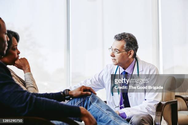 mature male doctor discussing with family while sitting in hospital lobby - critical illness stock pictures, royalty-free photos & images