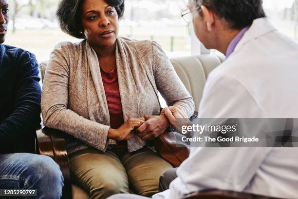 male doctor consoling mature woman sitting with son in hospital lobby - family hospital old stockfoto's en -beelden