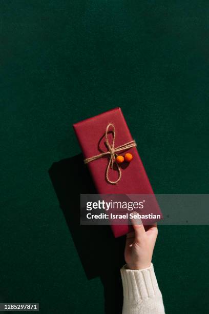 female hand holding christmas present in front of a green background - hand with gift stock pictures, royalty-free photos & images
