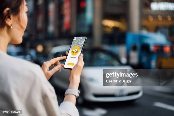 over the shoulder view of young asian businesswoman using mobile app device on smartphone to arrange a taxi pick up service in the city. speedy and trustworthy service. crowdsourcing and business on the go concept - over the shoulder view stock-fotos und bilder