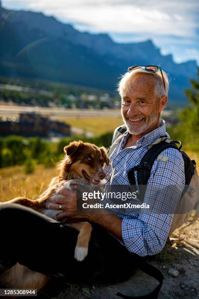 senior man sits with a dog on a leash in the mountains - distinguished gentlemen with white hair stock pictures, royalty-free photos & images