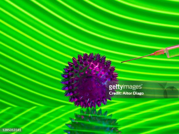 a syringe next to a micro organism. creative image. modern green background. - virus organism stock-fotos und bilder