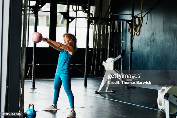 mature woman doing kettlebell swings during workout in gym - kugelhantel stock-fotos und bilder