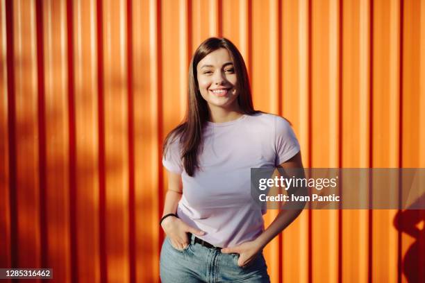 portret van een gelukkige jonge kaukasische vrouw die stelt - oranje achtergrond stockfoto's en -beelden