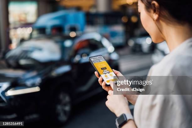 over the shoulder view of young asian businesswoman using mobile app device on smartphone to arrange a taxi pick up service in the city. speedy and trustworthy service. crowdsourcing and business on the go concept - over the shoulder view stock-fotos und bilder