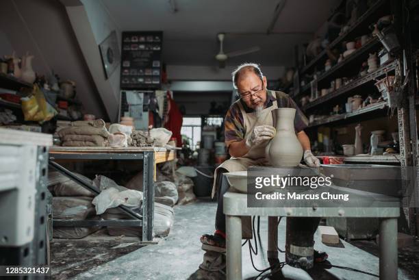 asian chinese senior man clay artist making pottery on a spinning pottery wheel in his craft studio - pottery making stock pictures, royalty-free photos & images
