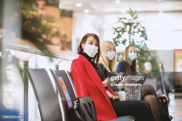 group of young people wearing protective face masks while waiting together in an airport lounge - airport mask stock pictures, royalty-free photos & images