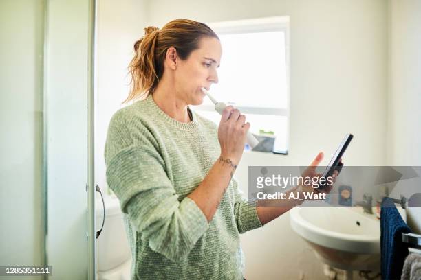 vrouw die haar tanden borstelt en haar telefoon in haar badkamers controleert - busy woman stockfoto's en -beelden