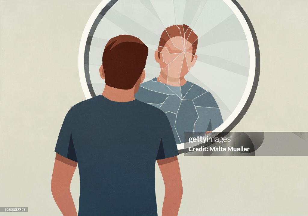 Young man looking into cracked mirror