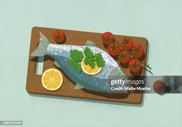 whole cooked fish with lemons and tomatoes on cutting board - tomato overhead stock illustrations