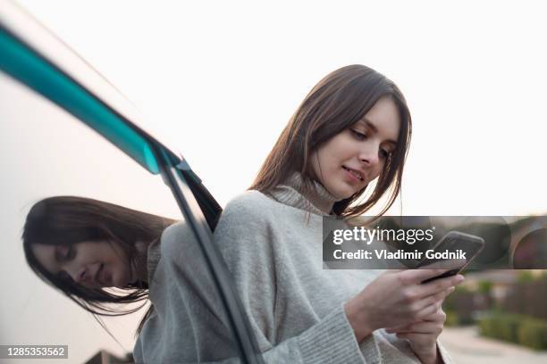 young woman using smart phone outside car - auto stehend stock-fotos und bilder