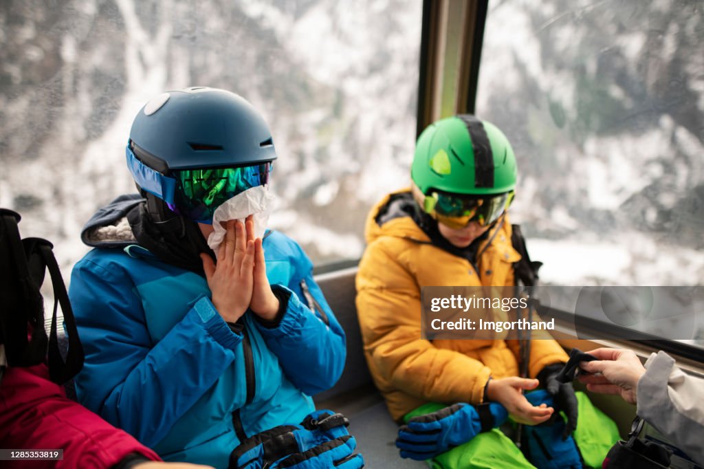 Kids sneezing in gondola ski lift ride.