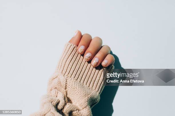 woman's hand in warm sweater showing manicure - gold nail polish stock-fotos und bilder