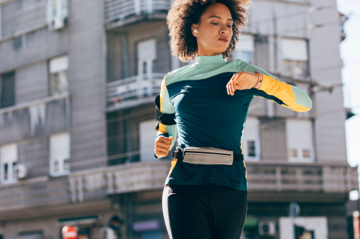 Young Afro American Woman Running in the Street while Checking her Smart Watch