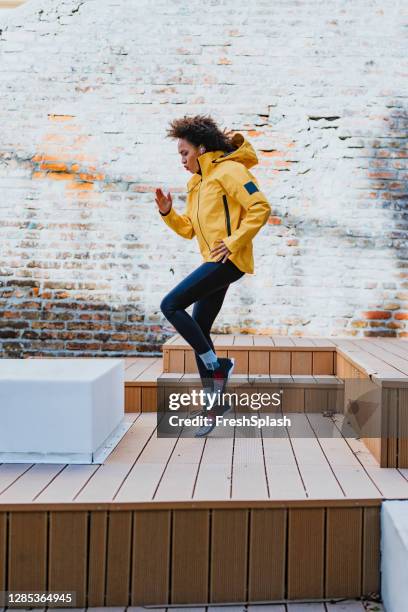 morning routine: fit afro american sportswoman in een gele track jas doet oefeningen buitenshuis - side view - geel jak stockfoto's en -beelden