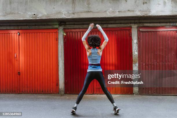 anonymous female athlete with an afro haircut doing jumping jacks outdoors - jumping jack stock pictures, royalty-free photos & images