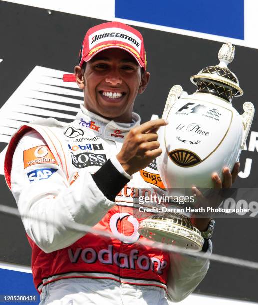 British McLaren Formula One driver Lewis Hamilton celebrates on the winners podium by raising the race winners trophy after winning the 2009...