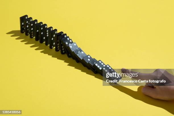 hand pushing at a row of dominoes - dominos falling stock pictures, royalty-free photos & images