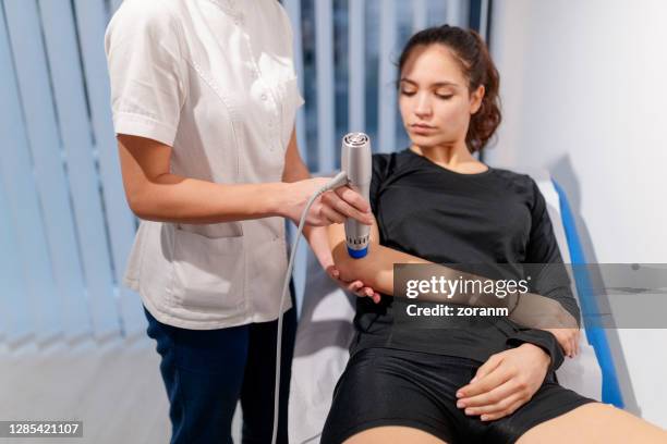 paciente femenina sometida a terapia de ondas en el codo lesionado - ondas electromagneticas fotografías e imágenes de stock