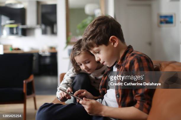 a brother and a sister looking at a tablet at home - children screen stock-fotos und bilder