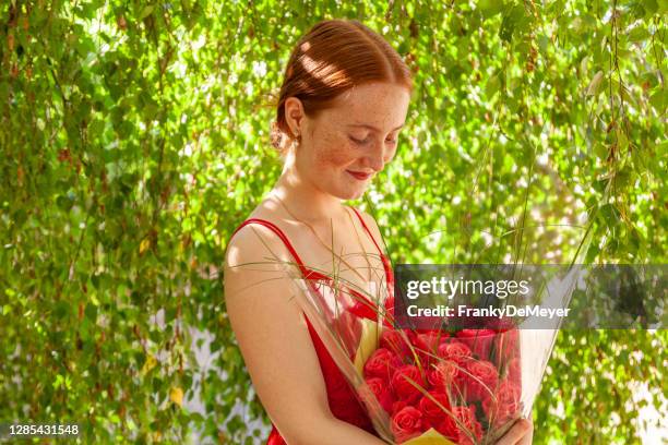 with copyspace provided, a teenage girl stands under a tree holding a birthday bouquet of red roses - 18th birthday stock pictures, royalty-free photos & images