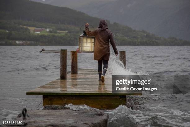 a person carrying a lantern on a dock in the rain - woman shower candle stock-fotos und bilder