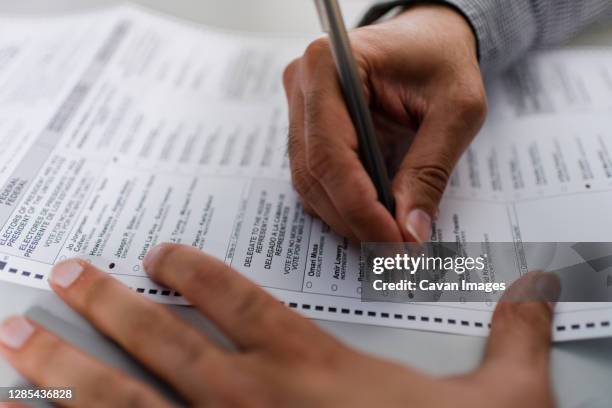 close up of man's hands completing absentee ballot for election - election ballot stock pictures, royalty-free photos & images