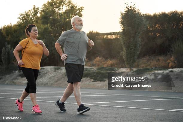 a woman and an elderly man are jogging in the street - fat guy running stock-fotos und bilder