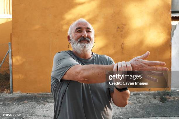 an elderly man with white hair and beard is stretching outdoors - chubby men stock-fotos und bilder