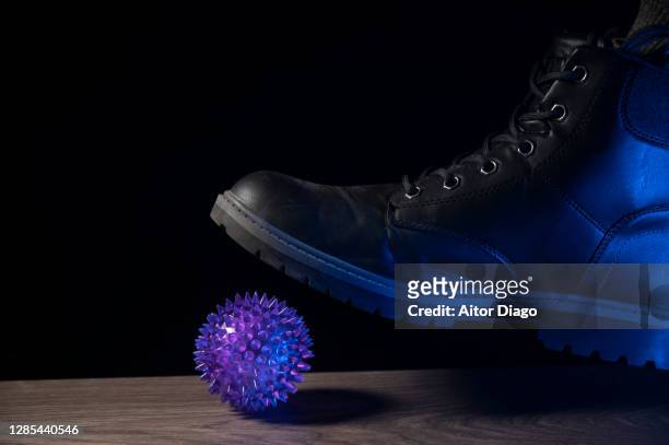 concept of elimination of the pandemic caused by the coronavirus: someone crushes the coronavirus by stepping on it with their boot. interpretation with humor of the extinction of the pandemic. - punt kick stock-fotos und bilder
