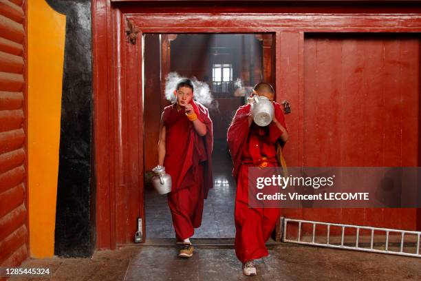 Deux moines tibétains en toge rouge sortent de la cuisine de leur monastère, avec une théière dans la main, décembre 2017, monastère de Litang,...