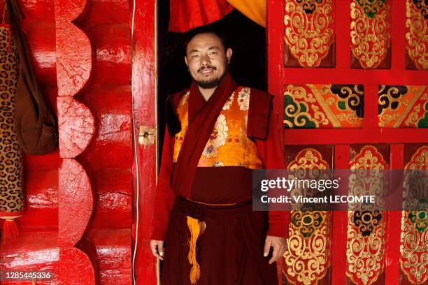 Portrait d'un moine tibétain en habits traditionnels, haut responsable d'un monastère au Sichuan, devant une porte en bois peint et sculpte, décembre...