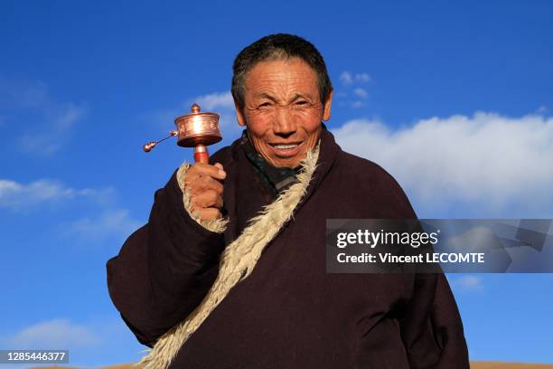 Portrait d'un homme tibétain souriant, faisant tourner moulin à prières sur fond de ciel bleu au Sichuan, décembre 2017, ville de Garze , Sichuan,...